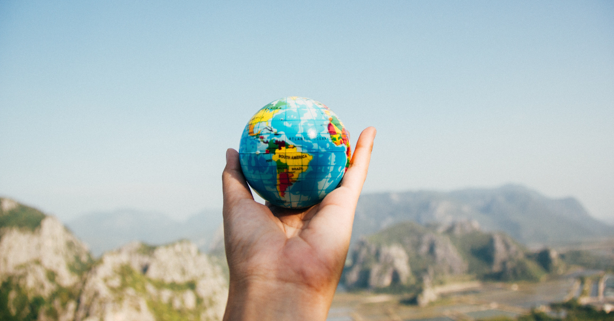 A hand holding up a small globe with mountains in the background